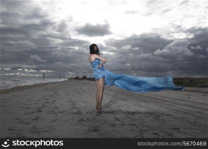 Caucasian model posing on the beach with long dress. Stormy sunset