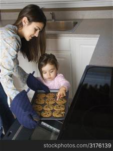 Caucasian mother and daughter taking cookies out of oven.