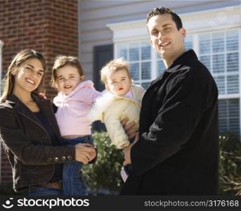 Caucasian mother and father with children standing in front of house.