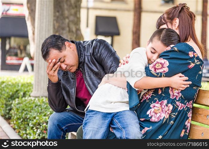 Caucasian Mother and Hispanic Father Comforting Mixed Race Son Outdoors.