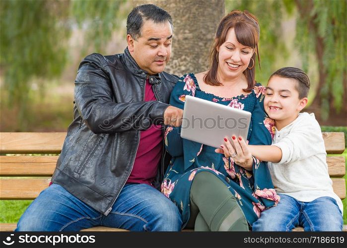 Caucasian Mother and Hispanic Father Using Computer Tablet With Mixed Race Son Outdoors.