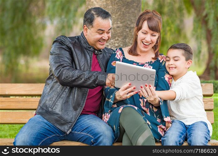 Caucasian Mother and Hispanic Father Using Computer Tablet With Mixed Race Son Outdoors.