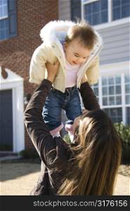 Caucasian mother holding up baby girl in front of house outside.