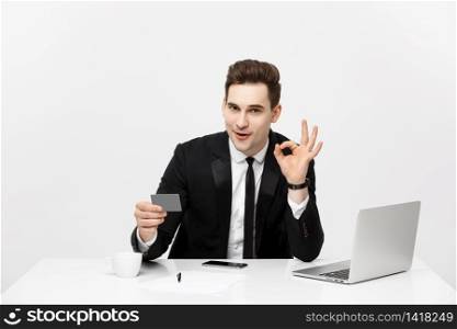 Caucasian office man in formal suit and tie demonstrating digital money in plastic credit card and showing ok isolated over gray background. Caucasian office man in formal suit and tie demonstrating digital money in plastic credit card and showing ok isolated over gray background.