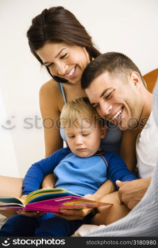 Caucasian parents and toddler son reading book.