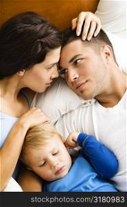 Caucasian parents cuddling with toddler son sleeping in bed.