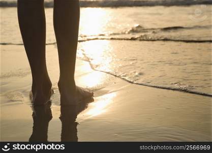 Caucasian person standing barefoot on beach in water.