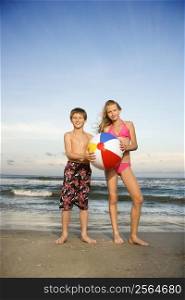 Caucasian pre-teen boy and girl holding beachball on beach.