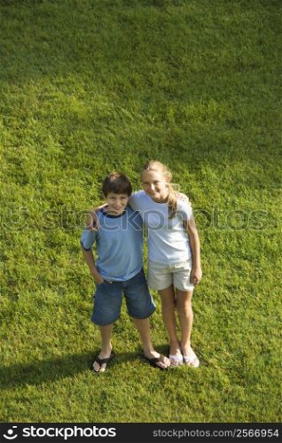Caucasian pre-teen boy and girl standing on lawn with arms around eachother.