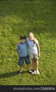 Caucasian pre-teen boy and girl standing on lawn with arms around eachother.