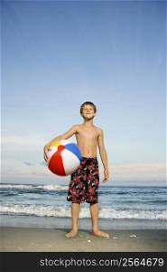 Caucasian pre-teen boy holding beachball on beach.