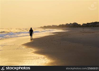 Caucasian pre-teen boy walking sihouette on beach at sunset.