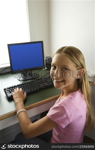 Caucasian pre-teen girl at computer looking over shoulder smiling at viewer.