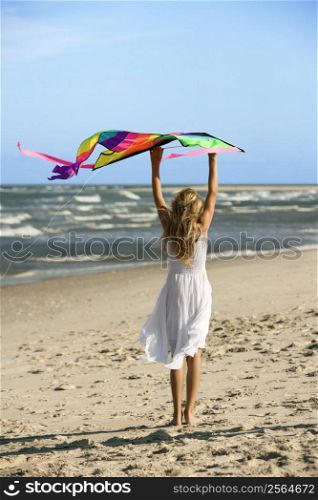 Caucasian pre-teen girl holding kite on beach.