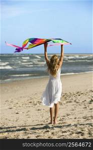 Caucasian pre-teen girl holding kite on beach.