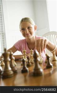 Caucasian pre-teen girl playing chess smiling.