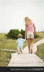 Caucasian pre-teen girl walking on beach access walkway and holding hands with Caucasian male toddler .