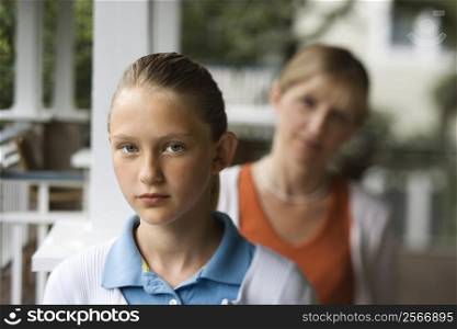 Caucasian pre-teen girl with mother behind her looking over shoulder.