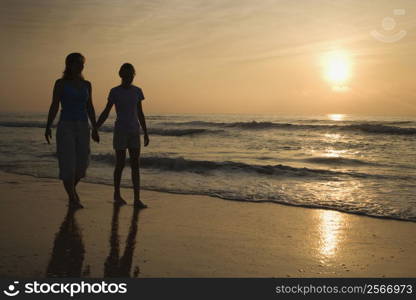 Caucasian prime adult female and female child walking on beach at sunset holding hands.