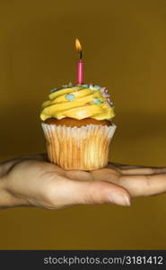 Caucasian prime adult female hand holding cupcake with lit candle.