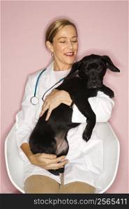Caucasian prime adult female veterinarian with black puppy.