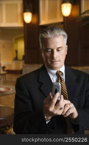 Caucasian prime adult male businessman dialing cellphone in hotel lobby.