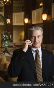 Caucasian prime adult male businessman talking on cellphone in hotel lobby.