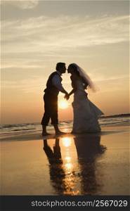 Caucasian prime adult male groom and female bride holding hands and kissing barefoot on beach at sunset.