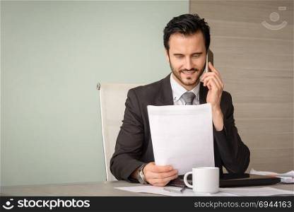 caucasian professional businessman using smartphone and reading financial report at office