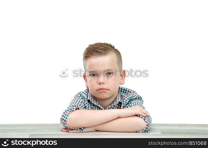 Caucasian school-age boy in a plaid shirt on a light isolated background sitting with his hands folded