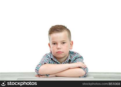 Caucasian school-age boy in a plaid shirt on a light isolated background sitting with his hands folded