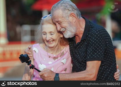 Caucasian Senior couples take selfie photos together at theme park and greeting family friends on camera	