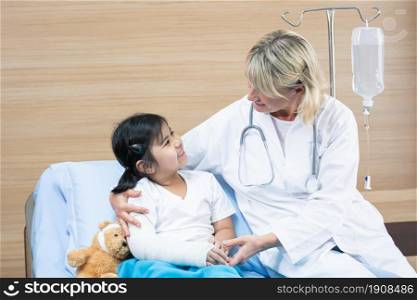 Caucasian senior doctor is wearing mask and check up patient, a girl who got a cast on her arm because of accident. Health, Hospital and Insurance Concept.