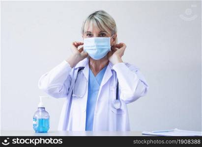 Caucasian senior doctor wearing mask and using gel for washing her hands. New Normal and Medical Concept.