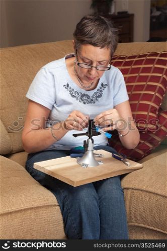 Caucasian senior lady starting to make a silver wire pendant in a vise or clamp