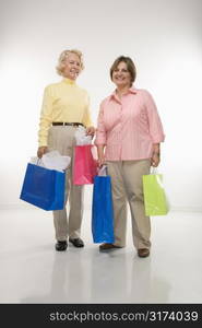 Caucasian senior woman and middle aged woman holding gift bags smiling at viewer.