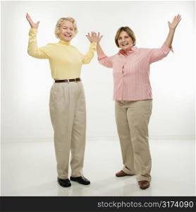 Caucasian senior woman and middle aged woman with arms in air.