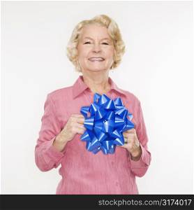Caucasian senior woman holding blue bow smiling at viewer.