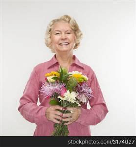 Caucasian senior woman holding bouquet of flowers and smiling at viewer.