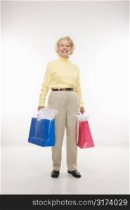 Caucasian senior woman holding gift bags smiling at viewer.