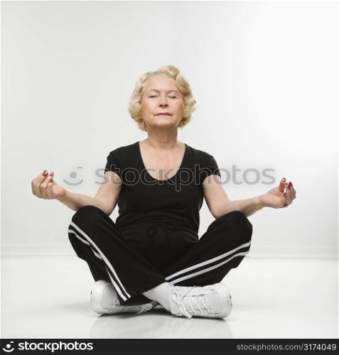 Caucasian senior woman sitting in yoga position on floor meditating.