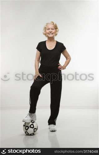 Caucasian senior woman standing with foot on soccer ball.