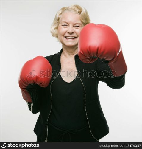 Caucasian senior woman wearing boxing gloves and throwing punch at viewer.