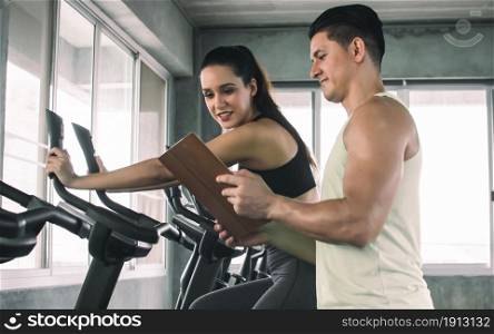 Caucasian sportive trainer is showing fitness program to a beautiful woman while doing exercise in gym. Sport and Healthy Concept.
