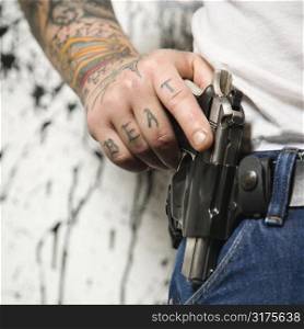Caucasian tattooed man wearing holster with gun.