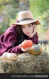 Caucasian teen girl  sitting in autumn park. She is holding orange pumpkin in her hands. Fall season