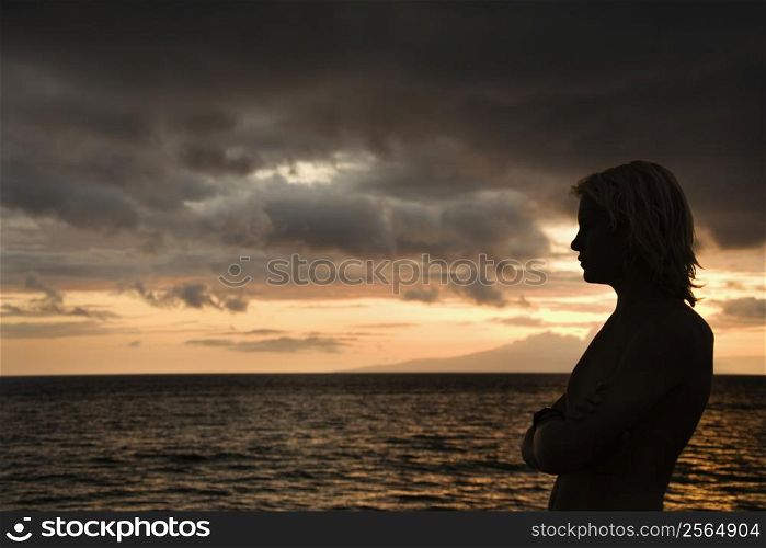 Caucasian teen male standing silhouetted on the shore of Maui, Hawaii, USA
