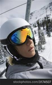 Caucasian teenage boy wearing helmet and goggles riding chair lift at ski resort.