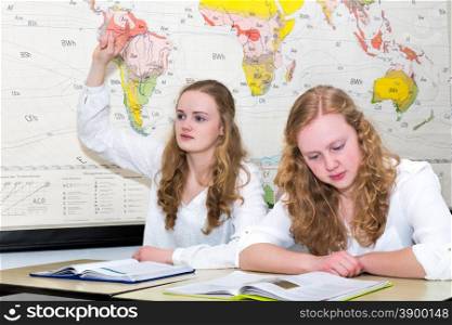 Caucasian teenage girl and student with learn finger in geography lesson in front of wall chart of the world