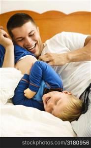 Caucasian toddler boy and father playing and tickling in bed.